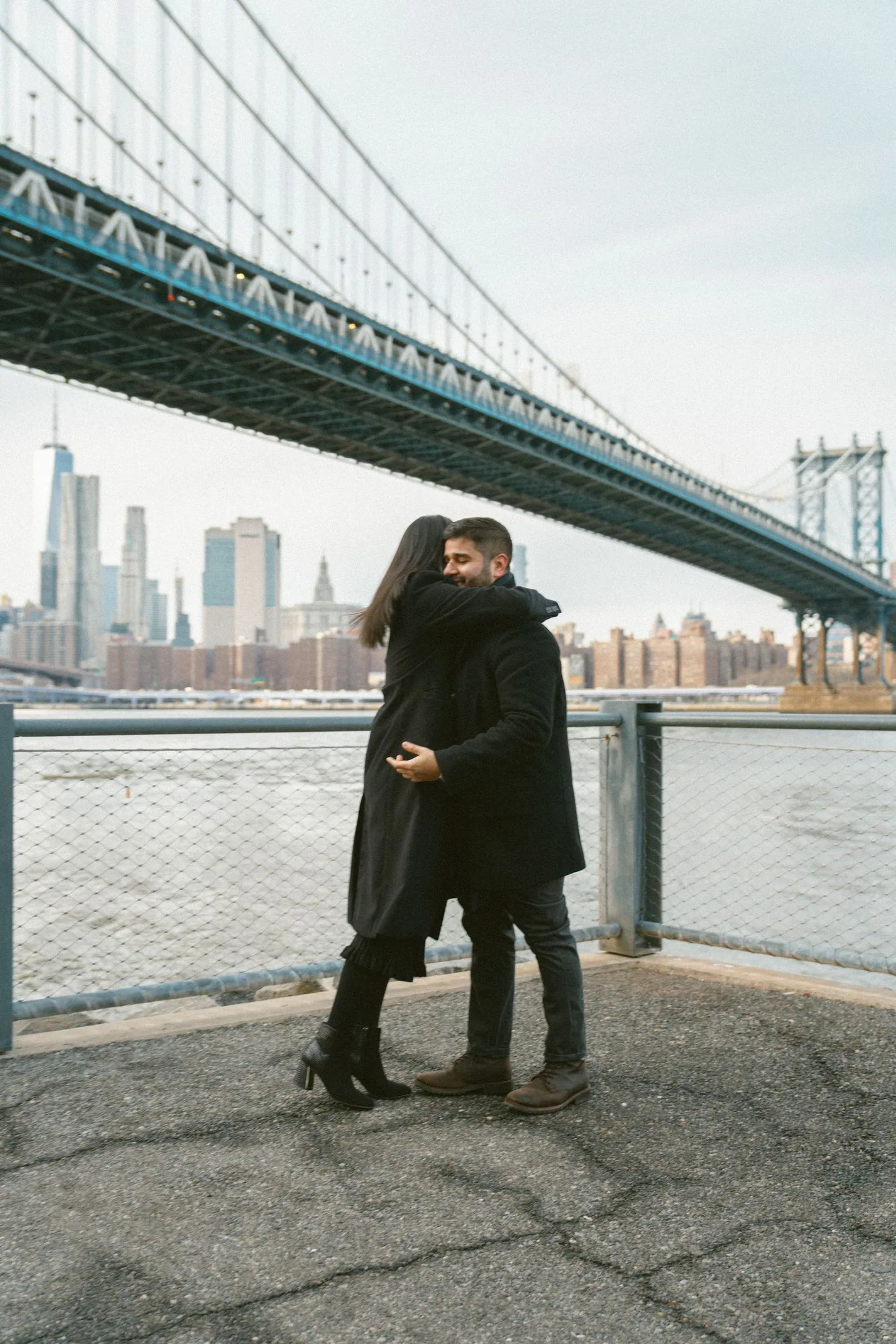 Couple embracing beneath the Manhattan Bridge in DUMBO